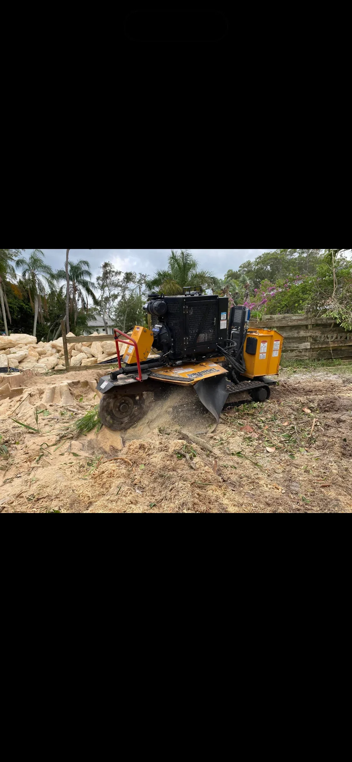 Yellow diesel wood chipper and grinder on cleared residential lot with debris piles
